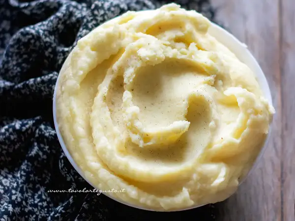 Una ciotola di cremoso pure di patate, guarnito con pepe nero macinato, su un tessuto scuro.