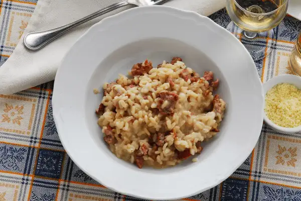 Un piatto di risotto alla pilota cremoso, con pezzetti di salsiccia, servito su una tovaglia a quadri.