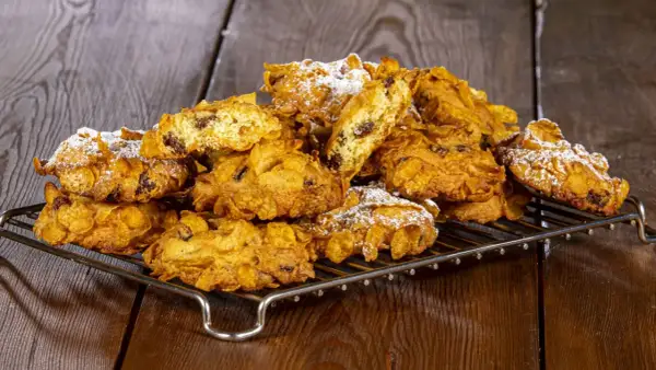 Biscotti croccanti, simili a rose del deserto, con uvetta e fiocchi di mais, spolverati di zucchero a velo su una griglia metallica.