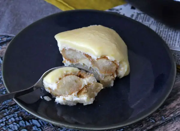 Una fetta di tiramisù al limone su un piatto blu, con un cucchiaino che ne preleva un assaggio.