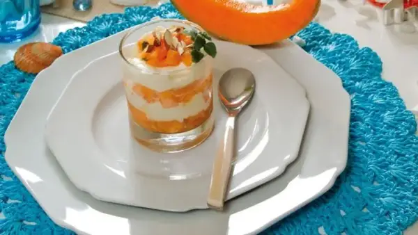 Delizioso semifreddo al melone a strati, guarnito con frutta fresca e mandorle, servito in un bicchiere su un piatto bianco.