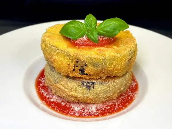 Due cordon bleu di melanzane impilati, dorati e croccanti, su un letto di salsa di pomodoro e basilico fresco.