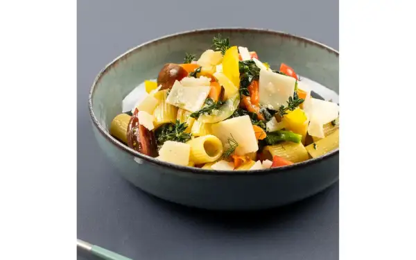 Piatto di pasta con verdure fresche, pomodorini, peperoni gialli e scaglie di parmigiano.