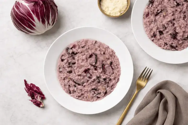 Un cremoso risotto al radicchio rosso, con un cespo intero e foglie sparse, pronto per essere gustato.