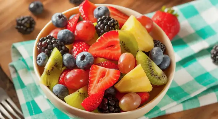 Una ciotola piena di macedonia di frutta colorata: fragole, mirtilli, lamponi, kiwi, ananas e uva.