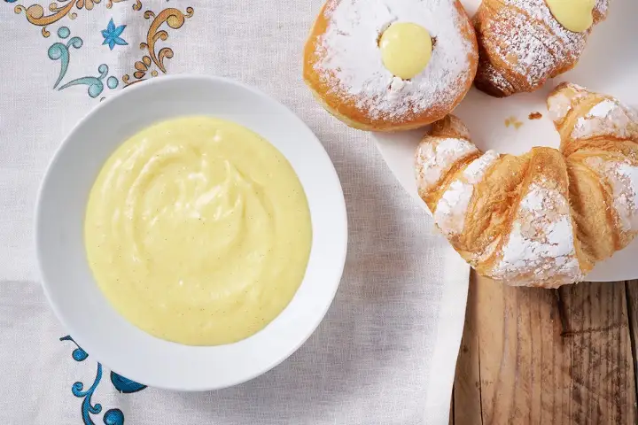 Una ciotola di crema pasticcera senza uova, perfetta per farcire croissant e bomboloni spolverati di zucchero a velo.